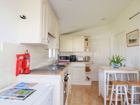 A kitchen with white cabinets appliances a small dining table with stools and a vase of yellow flowers at 224 Atlantic Bays in St Merryn