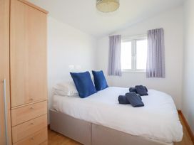 A bedroom with a double bed with blue pillows and towels next to a wooden wardrobe at 224 Atlantic Bays in St Merryn