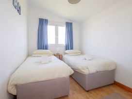 A bedroom with two single beds with white bedding blue curtains and a small table with a lamp between them at 224 Atlantic Bays in St Merryn