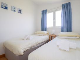 A bedroom with two single beds a small wooden bedside table with a lamp and blue curtains at 224 Atlantic Bays in St Merryn