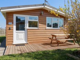 A small wooden house with white door and windows a wooden picnic table on a deck and a tree with yellow flowers at 224 Atlantic Bays in St Merryn