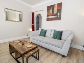 A living room with a gray sofa, wooden coffee tables, a mirror on the wall, and an abstract painting at Apartment 1 - Llandudno Central in Llandudno