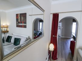 A living room area with a sofa and cushions reflected in a large mirror a red curtain beside an arched doorway leading to another room with wooden flooring at Apartment 1 - Llandudno Central in Llandudno