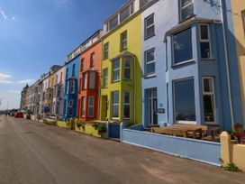 A row of colorful terraced houses along a street with outdoor benches at Enfys in Criccieth