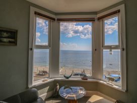 A sitting area with a glass table and decorative sea-themed items on the window sill overlooking the beach and sea at Enfys in Criccieth