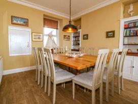 A dining room with a wooden table and chairs a hanging light and bookshelves at Enfys Criccieth
