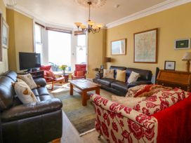 A living room with two black leather sofas a red patterned armchair wooden coffee table and a television by a window at Enfys in Criccieth