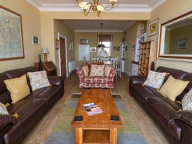 A living room with two dark leather sofas, a patterned armchair, a wooden coffee table, and a dining area at Enfys in Criccieth