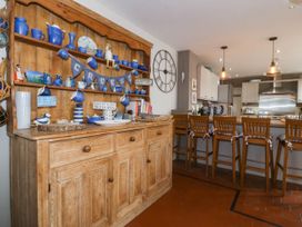 A kitchen with a wooden dresser holding blue ceramics and a breakfast bar with wooden stools at Enfys in Criccieth