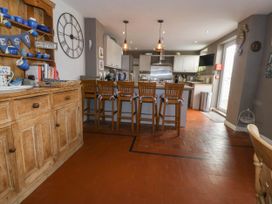 A kitchen with wooden chairs around an island and a wooden cabinet with blue dishes at Enfys Criccieth