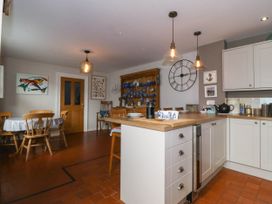 A kitchen with white cabinets a wooden countertop and a dining area with a wooden table and chairs at Enfys in Criccieth