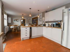 A kitchen with white cabinets wooden countertops pendant lights and a dining table with chairs at Enfys in Criccieth