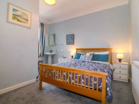 A bedroom with a wooden bed a patterned duvet two bedside tables with lamps and a sink at Enfys in Criccieth