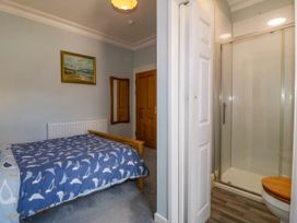 A bedroom with a bed covered in a blue bird patterned duvet a wooden door a mirror and an adjacent bathroom with a shower and toilet at Enfys Criccieth