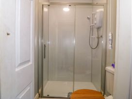 A small bathroom with a glass shower enclosure a white shower unit and a wooden toilet seat at Enfys in Criccieth
