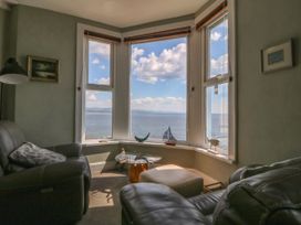 A sitting area with leather chairs and a table by bay windows overlooking water at Enfys in Criccieth