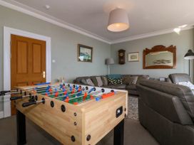 A living room with a foosball table a grey sectional sofa and a wooden door at Enfys in Criccieth