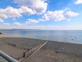 A beach with a concrete groyne extending into the sea under a blue sky with clouds at Enfys in Criccieth