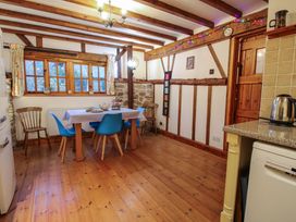 A dining area with a table covered by a tablecloth surrounded by wooden and blue chairs with wooden beams and a wooden door at Tawny Owl Barn in Leintwardine