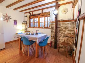 A dining area with a wooden table covered with a polka dot tablecloth and blue chairs in a room with wooden beams and stone wall at Tawny Owl Barn in Leintwardine