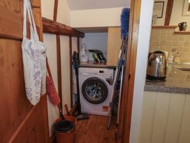 A small laundry area with a washing machine cleaning supplies and a mop bucket next to a wooden door at Tawny Owl Barn in Leintwardine