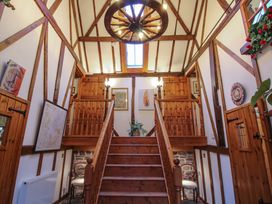 A wooden staircase with wooden railings in a hallway with exposed beams and a wagon wheel light fixture at Tawny Owl Barn in Leintwardine