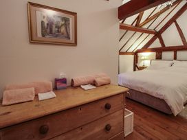 A bedroom with a wooden dresser with towels and a tissue box and a bed under exposed wooden beams at Tawny Owl Barn in Leintwardine