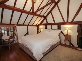 A bedroom with a double bed bedside tables with lamps wooden beams on the ceiling and a window with floral curtains at Tawny Owl Barn in Leintwardine