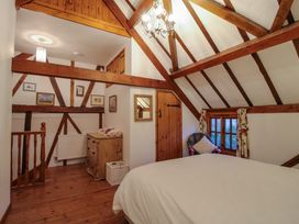 A bedroom with wooden beams a bed a dresser a chair and a window at Tawny Owl Barn in Leintwardine