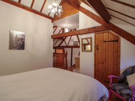 A bedroom with exposed wooden beams a bed a wooden door a chair with a cushion and a blanket and artwork on the wall at Tawny Owl Barn in Leintwardine