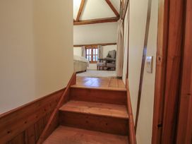 Wooden stairs leading to a bedroom with a bed a chair a rug and a window at Tawny Owl Barn in Leintwardine