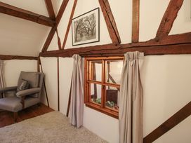 A room with exposed wooden beams a small window with curtains a gray armchair and a framed picture on the wall at Tawny Owl Barn in Leintwardine