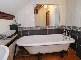A bathroom with a clawfoot bathtub next to a wall with black and white tiles and a large mirror at Tawny Owl Barn in Leintwardine