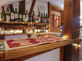 A wooden bar counter with a red and beige cloth runner and bottles of wine on a shelf behind at Tawny Owl Barn in Leintwardine