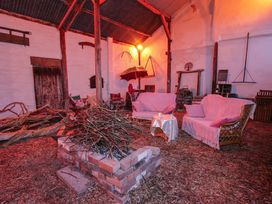 An indoor seating area with wicker sofas and a brick fire pit filled with sticks in a barn