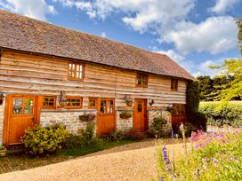An exterior view of a rustic wooden barn with stone foundation and flower beds by a gravel driveway at Tawny Owl Barn in Leintwardine
