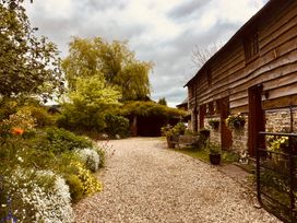 A gravel path with plants and flowers on one side and a wooden barn with stone base on the other at Tawny Owl Barn in Leintwardine