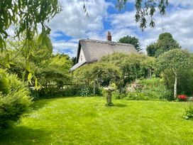 A garden with green grass trees and flowers and a thatched roof house in the background at Tawny Owl Barn in Leintwardine