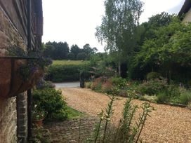 A garden with a gravel driveway and flowers next to a stone building with a field and trees in the background at Tawny Owl Barn in Leintwardine