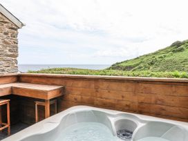 An outdoor area with a hot tub and wooden seating overlooking the ocean at 2 Cliff Cottages West Portholland near Gorran Haven