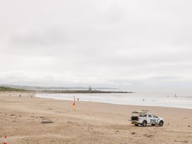 A beach with a lifeguard vehicle and surfers at 76A Mackworth Road Porthcawl