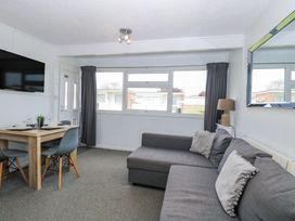 A living room with a gray sofa dining table with chairs wall-mounted TV and large window at California Summers in California Norfolk