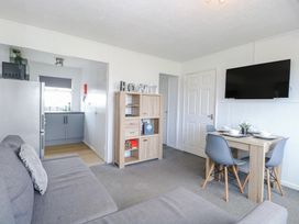 A living room with a grey couch a wooden shelf a dining table with four chairs and a wall mounted TV at California Summers in California Norfolk