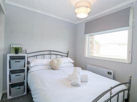 A bedroom with a metal bed frame white bedding towels on the bed a small shelving unit with storage baskets and a plant and a window with a blind at California Summers California Norfolk