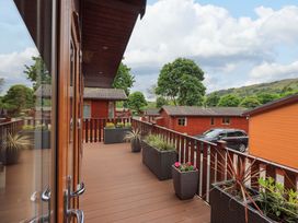 A wooden balcony with planters and a view of wooden cabins and trees at Pheasant's Nest Kirkstone 11 Limefitt Park near Windermere