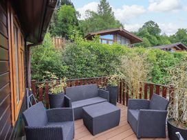 An outdoor deck with black wicker chairs and a table surrounded by potted plants and greenery at Pheasant's Nest Kirkstone 11 Limefitt Park near Windermere