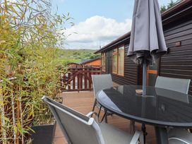 A wooden deck with a glass table and four chairs next to a house with wooden siding and plants in pots at Pheasant's Nest Kirkstone 11 Limefitt Park near Windermere