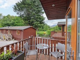 A small balcony with two chairs and a round table overlooking wooden cabins and trees at Pheasant's Nest Kirkstone 11 Limefitt Park near Windermere