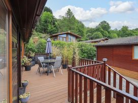 An outdoor wooden deck with a table and four chairs an umbrella and several potted plants surrounded by wooden railings at Pheasant's Nest Kirkstone 11 Limefitt Park near Windermere