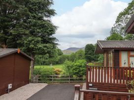 A wooden cabin with a deck and railing next to a wooden shed with trees and hills in the background at Pheasant's Nest Kirkstone 11 Limefitt Park near Windermere